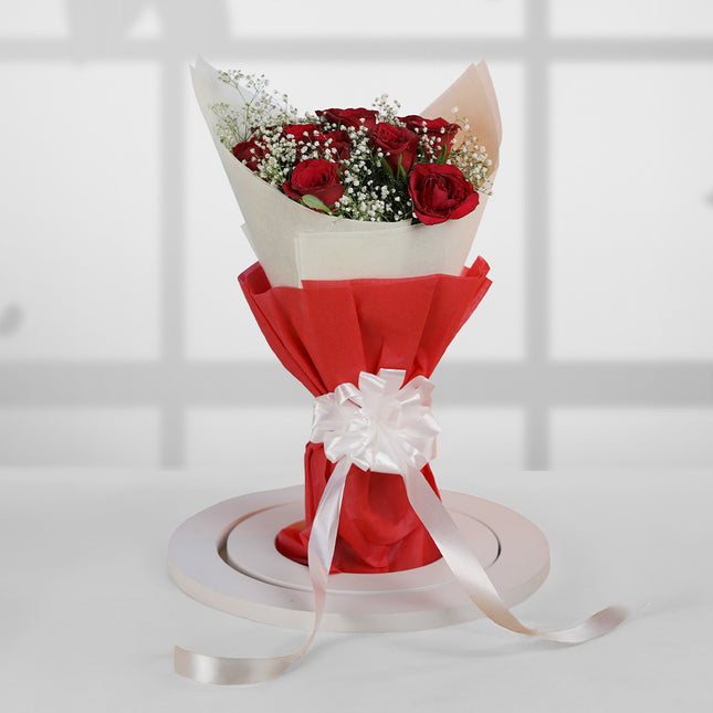 Bouquet of red roses with baby's breath, wrapped in red paper and white ribbon, on table