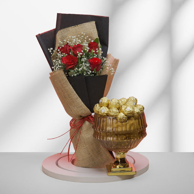 Bouquet of red roses with baby's breath and golden-wrapped chocolates in a glass bowl