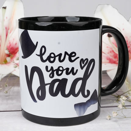 Black coffee mug with 'love you Dad' text, top hat, bow tie, and flowers in background