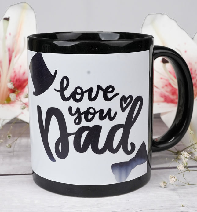 Black coffee mug with 'love you Dad' text, top hat, bow tie, and flowers in background