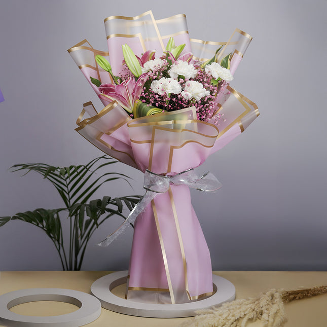Elegant pink and white flower bouquet with gold-trimmed wrap and ribbon on a table