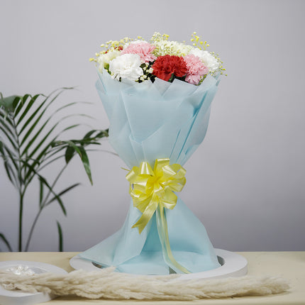 Colorful carnation bouquet in blue wrapping with yellow ribbon, gift arrangement on table