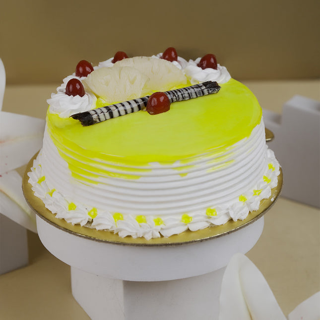 Round pineapple cake with yellow glaze, cherries, whipped cream, chocolate sticks on white stand