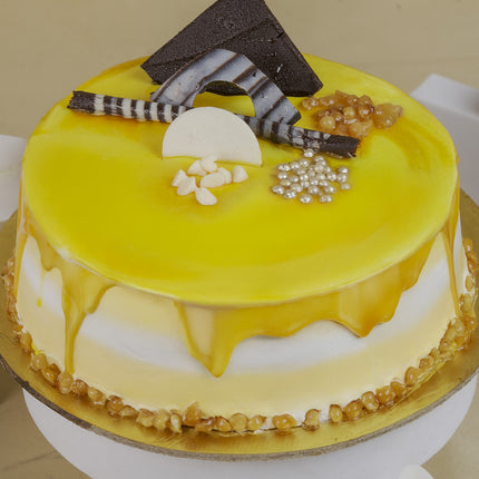 Yellow glazed cake with white frosting, chocolate decorations, silver pearls, and caramel nuts