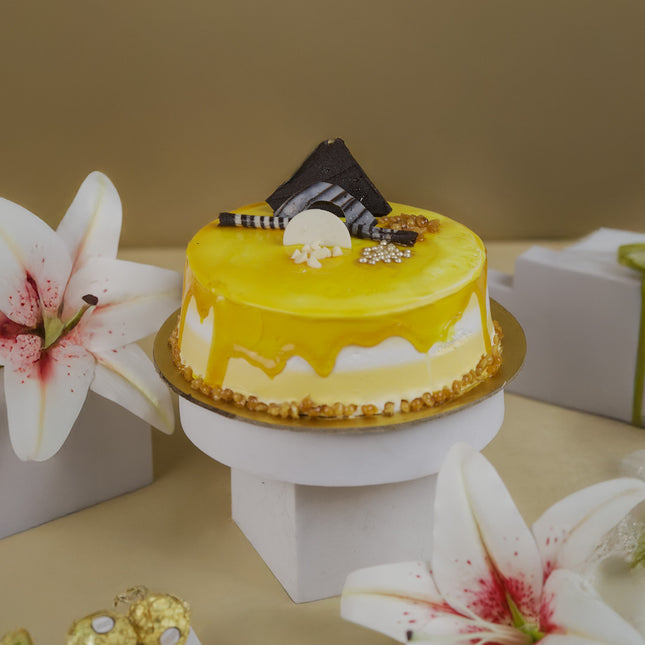 Yellow glazed cake with chocolate decorations on a stand, surrounded by white lilies and gifts