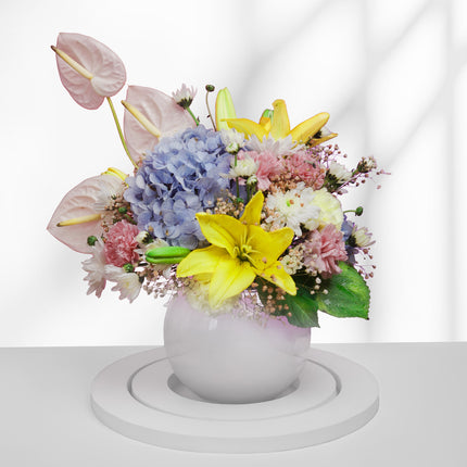 Colorful flower arrangement with lilies, hydrangeas, and anthuriums in a white round vase