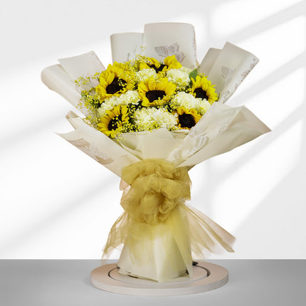 Bouquet of yellow sunflowers and white flowers wrapped in cream paper with yellow ribbon