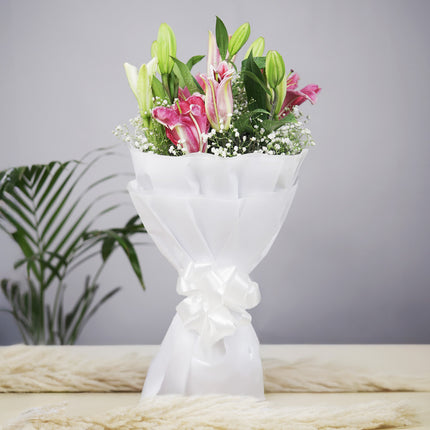 Elegant bouquet of pink and white lilies wrapped in white paper with ribbon on a table