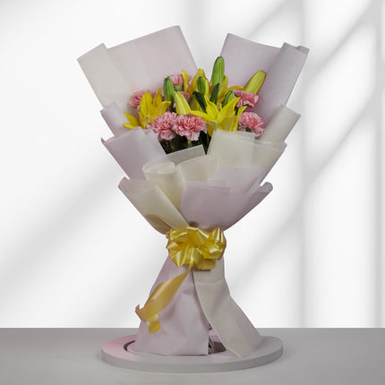 Bouquet of pink carnations and yellow lilies wrapped in white paper with a yellow ribbon