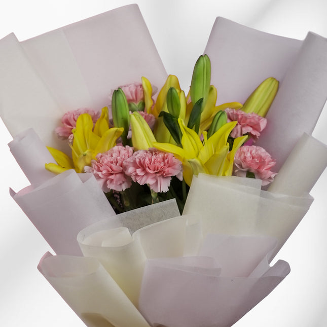 Bouquet of yellow lilies and pink carnations wrapped in white paper