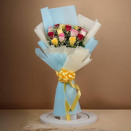 Bouquet of mixed roses in red, yellow, and pink wrapped in blue paper with yellow ribbon