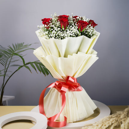 Bouquet of red roses and white baby's breath wrapped in cream paper with red ribbon