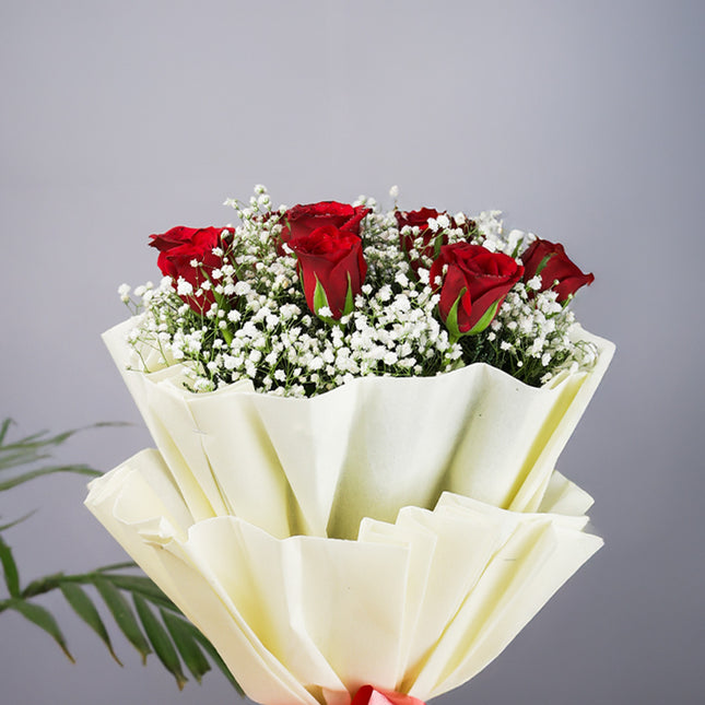 Bouquet of red roses and white baby's breath wrapped in cream paper against gray background