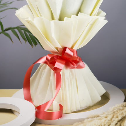 Bouquet wrapped in cream tissue paper with red satin ribbon on a table, floral arrangement