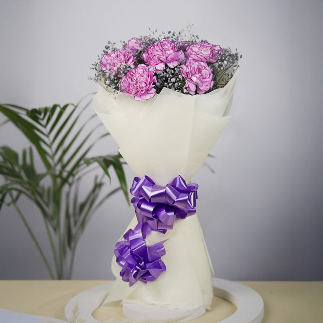 Bouquet of pink carnations with baby's breath, wrapped in cream paper with purple bows