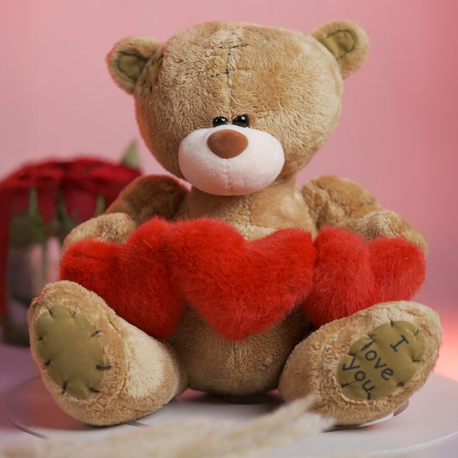 Plush teddy bear holding red hearts with 'I love you' on paw, romantic gift setting