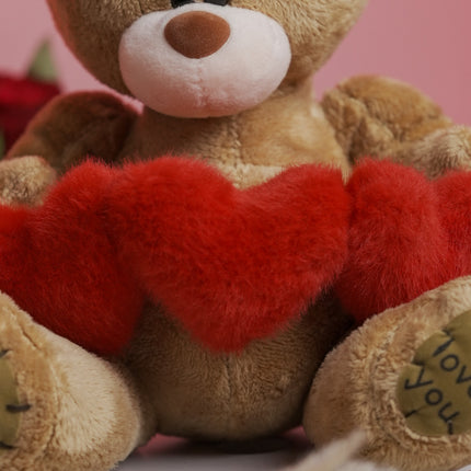 Brown teddy bear holding red heart plush, 'love you' embroidered on paw, pink background