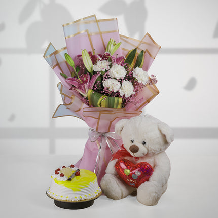 Bouquet of lilies and carnations with a teddy bear and lemon cake on white background