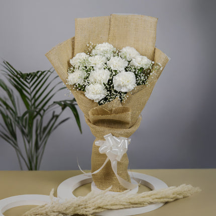 White carnation bouquet wrapped in burlap with ribbon, floral arrangement on table