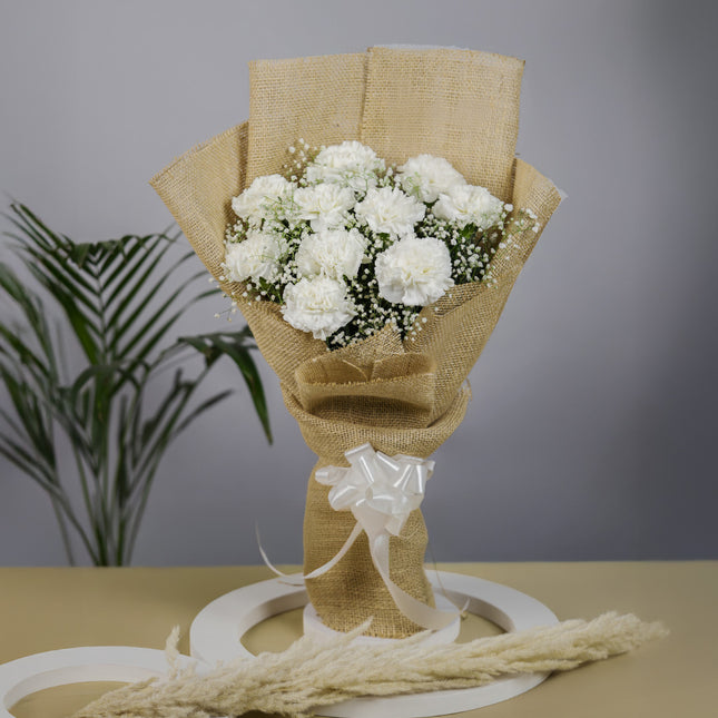White carnation bouquet wrapped in burlap with ribbon, floral arrangement on table